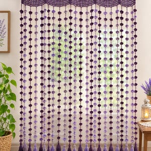 May include: A decorative crochet curtain featuring a scalloped top border with wooden buttons, hanging in vertical strands of small purple and lavender flowers. Each strand ends in a yarn tassel, creating a layered, textured window treatment.