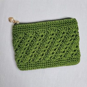 Può includere: Una pochette rettangolare all'uncinetto color verde oliva con un motivo testurizzato a punto conchiglia diagonale. L'accessorio presenta una cerniera scura sul bordo superiore, rifinita con un piccolo tirazip in metallo dorato a forma di cuore.