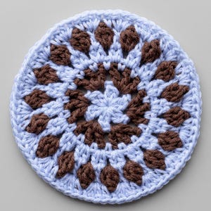 May include: A circular crochet coaster featuring a light blue yarn base with a repeating pattern of dark brown puff stitches arranged in two concentric rings around a central light blue star-shaped motif, finished with a simple blue border.