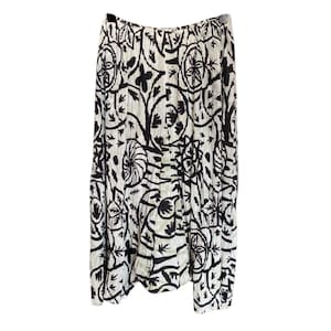 May include: A pleated midi skirt featuring a high-contrast black and white botanical print. The garment has an elasticated waistband and a flowing, A-line silhouette with a repeating pattern of stylised leaves, flowers, and circular motifs.