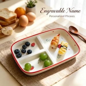 Puede incluir: Un plato rectangular de cerámica blanca dividido con borde rojo, con pequeñas ilustraciones de fresas y hojas. El plato contiene arándanos, uvas verdes y dos piezas de sushi. El texto dice: Engravable Name Personalized Phrases.