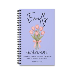 Puede incluir: Un cuaderno de espiral color morado claro con el nombre Emilly en letra cursiva negra, un ramo de tulipanes rosas atado con un lazo rosa y el texto GUÁRDAME COMO A LA NIÑA DE TUS OJOS; ESCÓNDEME BAJO LA SOMBRA DE TUS ALAS SALMOS 17:8.
