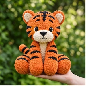 May include: A crocheted tiger plush toy featuring bright orange yarn with black stripes, a cream-colored muzzle, and large black safety eyes. The stuffed animal has rounded ears, a small black nose, and a visible tail, crafted with a soft, textured yarn.