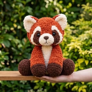 Puede incluir: Un peluche de panda rojo hecho de hilo suave y texturizado. El juguete presenta un cuerpo de color naranja óxido, pecho y cara de color crema, manchas de color marrón oscuro alrededor de los ojos y patas de color marrón oscuro. Tiene orejas.