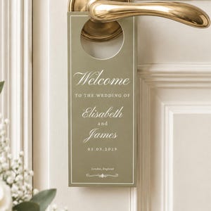 May include: An olive green rectangular door hanger with white text that reads Welcome TO THE WEDDING OF Elisabeth and James 05.05.2029 London, England. The hanger features a circular cutout at the top and is displayed on a brass-colored door handle.
