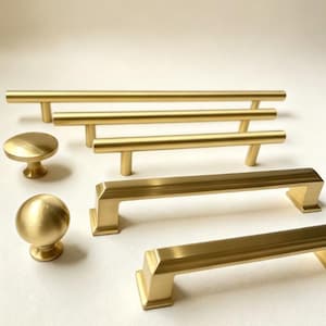 May include: A collection of brushed gold cabinet hardware including three cylindrical bar pulls of varying lengths, one round knob with a flat top, and one spherical knob, alongside two rectangular bar pulls with angled ends and a brushed finish.