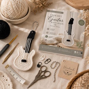 May include: A crochet guitar keychain with a cream body and black neck, a printed pattern booklet titled Crochet Guitar Keychain, a 2.5 mm crochet hook, a metal measuring tape, scissors, stitch markers, a ball chain, and a handmade tag.