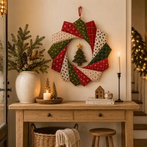 May include: A circular fabric wreath featuring a patchwork design of red, green, and cream-colored segments with snowflake and plaid patterns. A small, three-dimensional green fabric Christmas tree with a yellow star hangs in the center.
