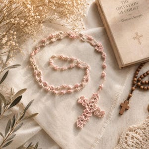 Peut inclure: Un chapelet en crochet rose clair fait main, composé d'une série de petites perles circulaires interconnectées et d'une croix en crochet détaillée et ajourée à l'extrémité, disposé en forme de cercle sur un tissu de couleur claire.
