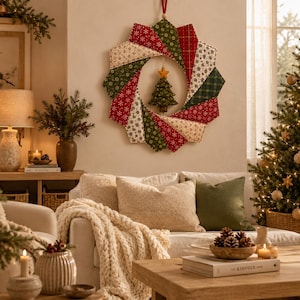 May include: A circular fabric wreath featuring a star-patterned design in red, green, and cream colors. The wreath is constructed from folded fabric segments and includes a small, stuffed fabric Christmas tree ornament hanging in the center.