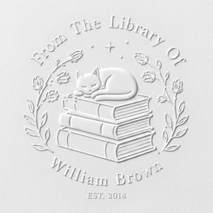 May include: A white embossed stamp design featuring a sleeping cat resting on a stack of three books. The text reads From The Library Of William Brown EST. 2018, surrounded by a circular frame of floral vines and small stars on a white background.
