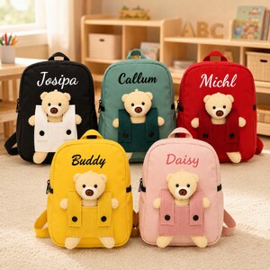 Pode incluir: Cinco mochilas nas cores preta, verde-azulado, vermelha, amarela e rosa, cada uma com um urso de pelúcia num bolso de veludo cotelê correspondente. Os nomes Josipa, Callum, Michl, Buddy e Daisy estão bordados em letra cursiva branca ou preta.