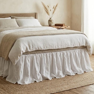 Può includere: Una balza per letto in lino bianco con un design a volant arricciato. La balza presenta una caduta lunga e fluida che raggiunge il pavimento, offrendo un aspetto pulito e stratificato sotto un copripiumino in lino bianco e cuscini abbinati.