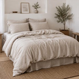 Puede incluir: Una funda nórdica de lino beige con un acabado de tela texturizada y una fila de botones redondos visibles a lo largo del borde inferior. El juego de cama incluye dos fundas de almohada rectangulares a juego para un aspecto neutro.
