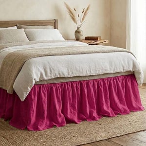 May include: A vibrant fuchsia pink bed skirt featuring a gathered, ruffled design that extends from the base of the mattress to the floor. The fabric has a visible textured weave, providing a bold contrast to the neutral bedding above it.