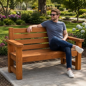 May include: A sturdy wooden bench with a slatted backrest and seat, featuring a warm brown finish and visible wood grain. The bench is constructed with thick, rectangular support posts and horizontal planks, providing a stable seating surface.