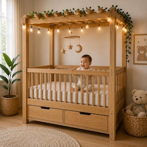 May include: A light-colored wooden canopy crib with two storage drawers at the base, featuring a string of warm globe lights and green vines draped across the top frame, with a hanging mobile of stars and a moon suspended above the mattress.