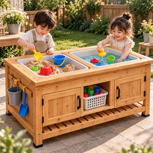 Pode incluir: Uma mesa sensorial de madeira com duas bandejas de plástico removíveis, uma cheia de areia e a outra com água. A mesa inclui uma prateleira inferior, dois armários de armazenamento com puxadores pretos e ganchos laterais para um balde cinza.
