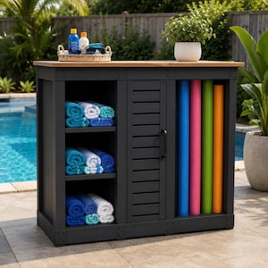 May include: A dark gray outdoor storage cabinet with a light wood top, featuring three open shelves stacked with folded blue and white towels, a central louvered door, and a side compartment holding four vertical rolled mats in blue, pink, green, and orange.