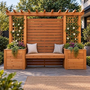 May include: A wooden garden bench with a high horizontal slat backrest and an overhead pergola frame. Two square planters are attached to the sides, featuring lattice panels with climbing white flowers and green foliage. Two throw pillows sit on the seat.