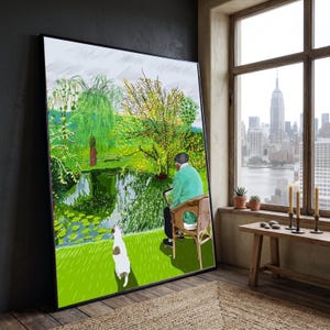 Può includere: Una grande stampa artistica incorniciata che raffigura una persona con un maglione verde seduta su una sedia di vimini, intenta a dipingere un paesaggio con uno stagno, un salice piangente e ninfee. Un piccolo cane bianco è sull'erba verde brillante.
