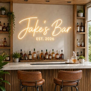 Könnte beinhalten: Ein individuelles Neonschild an einer Wand mit der Aufschrift Jake's Bar in einer leuchtend gelben Schreibschrift und dem Text EST. 2026 in einer kleineren Blockschrift darunter. Das Schild befindet sich über einer hölzernen Bartheke.