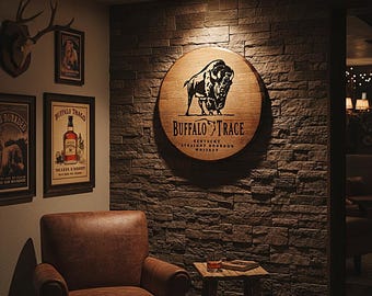 May include: A circular wooden sign featuring a black buffalo graphic and the text Buffalo Trace Kentucky Straight Bourbon Whiskey mounted on a dark stone wall above a brown leather armchair and a small wooden side table with a glass of amber liquid.