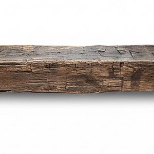 May include: A long, rectangular wooden beam with a dark brown, weathered finish. The surface displays a rough, textured grain with visible cracks, knots, and indentations throughout the length of the timber, showing a natural, aged appearance.