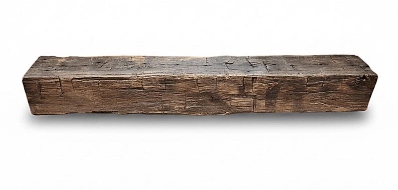 May include: A long, rectangular wooden beam with a dark brown, weathered finish. The surface displays a rough, textured grain with visible cracks, knots, and indentations throughout the length of the timber, showing a natural, aged appearance.