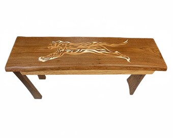 May include: A rectangular wooden bench featuring a live edge top with a natural brown finish. The surface is inlaid with a lighter-colored wood design depicting a leaping big cat in profile. The bench is supported by four angled wooden legs.