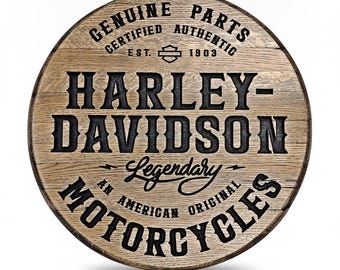 May include: A circular wooden sign with a natural light brown wood grain finish. The text reads GENUINE PARTS CERTIFIED AUTHENTIC EST. 1903, HARLEY-DAVIDSON, Legendary, AN AMERICAN ORIGINAL, and MOTORCYCLES in black, embossed-style lettering.