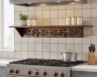May include: A dark wood floating wall shelf featuring a carved grape vine and leaf pattern on the front edge. The shelf is mounted above a stainless steel gas range with six burners, red control knobs, and a matching stainless steel range hood.