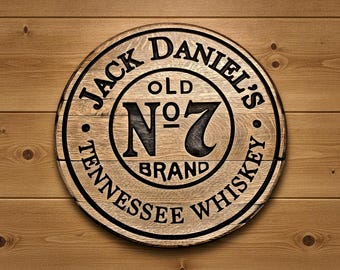May include: A circular wooden sign featuring the black engraved Jack Daniel's Old No. 7 Tennessee Whiskey brand logo. The design includes the text Jack Daniel's, Old No. 7, and Tennessee Whiskey arranged in a circular pattern on a light brown wood grain.