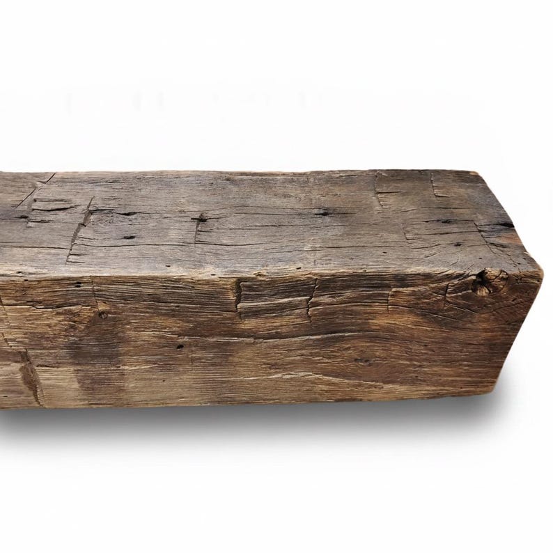 May include: A rectangular wooden beam with a weathered, dark brown finish. The surface displays a rough, textured grain with visible cracks, knots, and deep fissures running along the length of the timber, showcasing a natural, aged appearance.