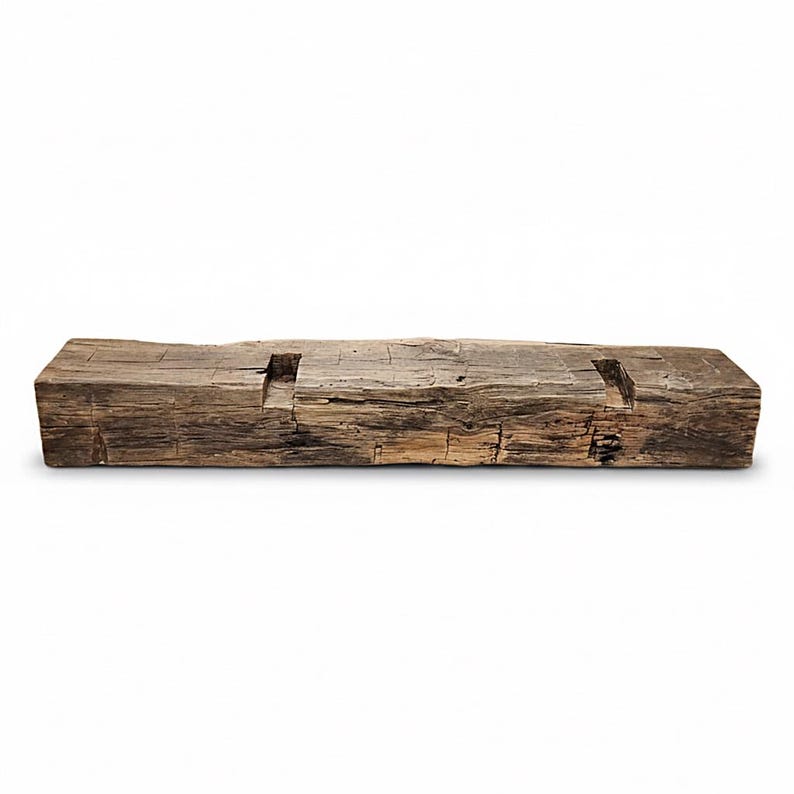 May include: A rectangular piece of reclaimed wood with a weathered, dark brown finish and a rough, textured surface. The top side features two evenly spaced, rectangular cutouts carved into the wood, showing natural grain and deep cracks.