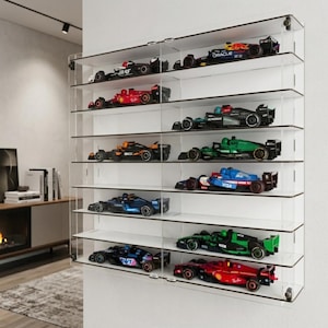 Peut inclure: Une vitrine murale en acrylique transparent dotée de plusieurs étagères horizontales. À l'intérieur, douze voitures de course miniatures de Formule 1 de différentes couleurs, dont rouge, noir, vert et bleu, sont disposées sur les étagères.