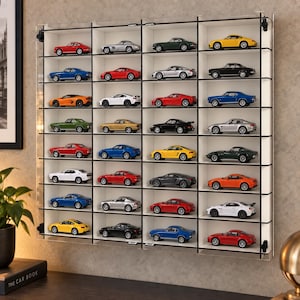 May include: A wall-mounted clear acrylic display case featuring four vertical columns and eight horizontal shelves, housing thirty-two miniature die-cast model cars in various colors including red, blue, yellow, silver, black, white, orange, and green.