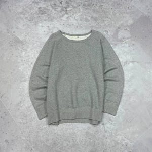 May include: A heather gray long-sleeve sweatshirt featuring a crew neckline, raglan sleeves, and ribbed cuffs and hem. The interior collar displays a small white label with black text. The garment is constructed from a solid-colored knit fabric.