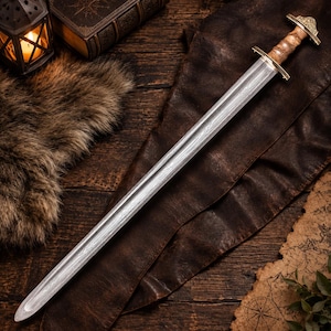 May include: A double-edged sword featuring a patterned Damascus steel blade with a central fuller. The hilt is crafted from light brown wood with a polished brass crossguard and a matching brass pommel featuring intricate engraved detailing.