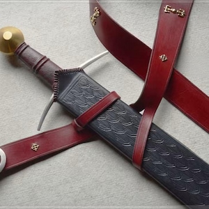 May include: A sword with a dark brown leather-wrapped handle and a round brass pommel, housed in a black scabbard featuring a textured scale pattern. The scabbard is secured by a deep red leather belt with a silver-toned buckle and small brass accents.