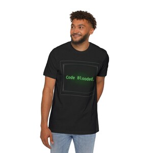May include: A black short-sleeved t-shirt featuring a graphic of a vintage computer monitor screen in the centre. The screen displays the text "Code Blooded_" in a bright green, pixelated font against a dark, glowing green background.