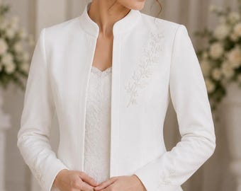 May include: A white long-sleeved bolero jacket featuring a mandarin collar and delicate silver-toned leaf embroidery on the left chest and cuffs. The jacket is worn over a white lace dress, creating a structured and elegant layered appearance.
