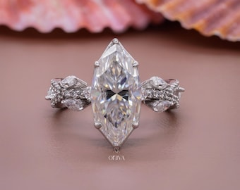 Op de afbeelding: Een zilverkleurige ring met een grote marquise-geslepen middensteen die door zes pootjes wordt vastgehouden. De band is versierd met kleinere marquise-geslepen stenen en pavé-accenten aan de zijkanten. Het woord OLIVA staat onderaan.