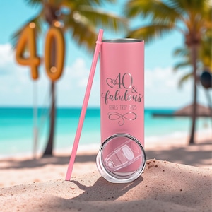 Puede incluir: Un vaso t&eacute;rmico rosa con una pajita a juego y una tapa transparente. El vaso tiene el texto "40 & fabulous GIRLS TRIP 2025" en una fuente cursiva. El fondo muestra una escena de playa con palmeras y el n&uacute;mero 40.