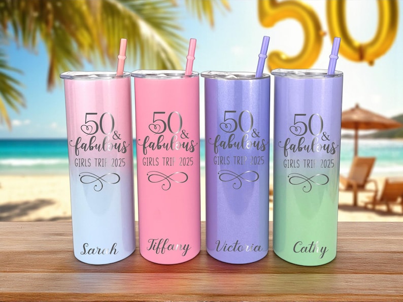 K&ouml;nnte beinhalten: Vier bunte Isolierbecher mit Strohhalmen, jeweils mit dem Text "50 & fabulous GIRLS TRI 2025" und einem Namen. Die Becher sind in Rosa, Lila, Blau und Gr&uuml;n gehalten, mit einer Strandkulisse im Hintergrund.