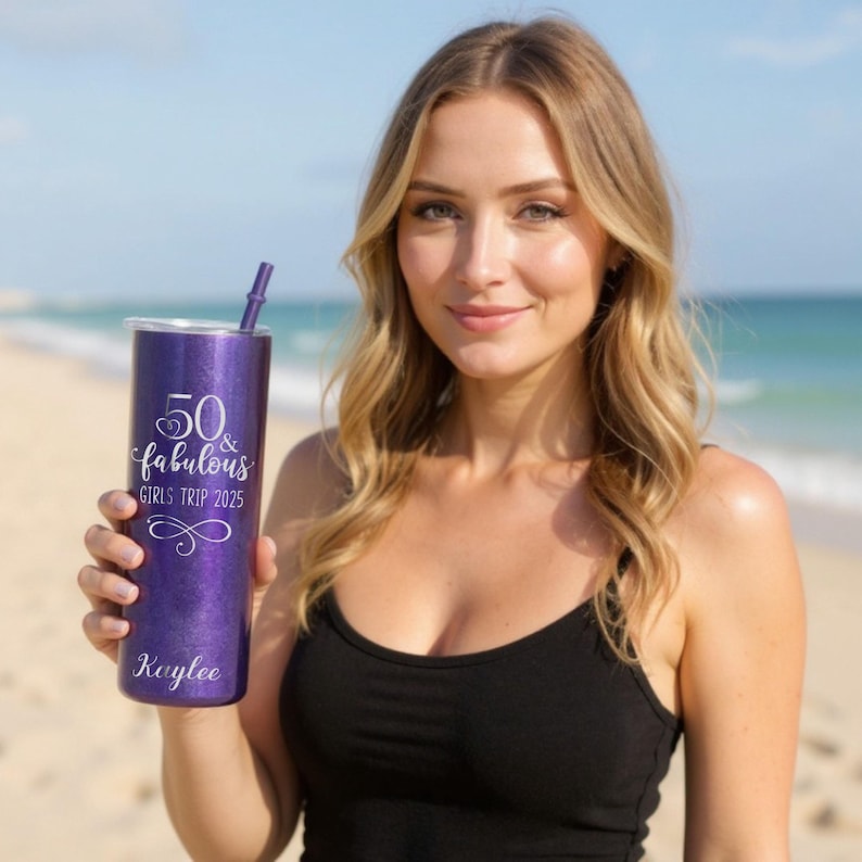 K&ouml;nnte beinhalten: Ein lila Glitzerbecher mit Strohhalm, mit dem Text "50 & Fabulous GIRLS TRIP 2025" und dem Namen "Kaylee". Der Becher ist zylindrisch und hat einen silbernen Deckel. Der Hintergrund ist ein Strand mit dem Meer.