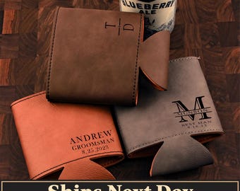 May include: Three leather can coolers in brown, tan, and grey. The brown cooler features the initials T and D. The tan cooler is engraved with ANDREW, GROOMSMAN, and 8.25.2023. The grey cooler displays the letter M, MUNSON, BEST MAN, and 8.16.23.