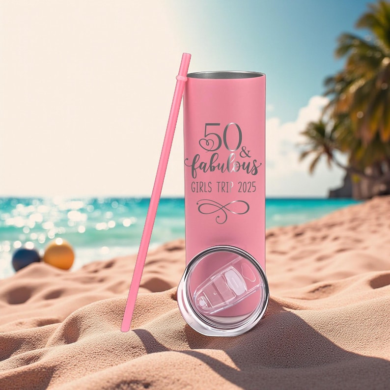 K&ouml;nnte beinhalten: Ein rosa isolierter Becher mit einem passenden rosa Strohhalm. Auf dem Becher steht in silberner Schrift der Text "50 & fabulous GIRLS TRIP 2025". Der Deckel ist transparent und der Becher steht an einem Sandstrand mit dem Meer im Hintergrund.