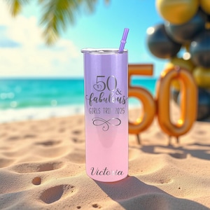 K&ouml;nnte beinhalten: Ein Edelstahlbecher mit einem Farbverlauf in Lila und Rosa. Er hat einen Deckel und einen lila Strohhalm. Der Text auf dem Becher lautet "50 & fabulous GIRLS TRIP 2025" und "Victoria". Der Hintergrund zeigt eine Strandszene mit Ballons.