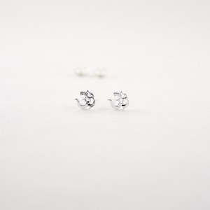 May include: A pair of silver Om symbol earrings. The earrings are small and delicate, and they are perfect for everyday wear.
